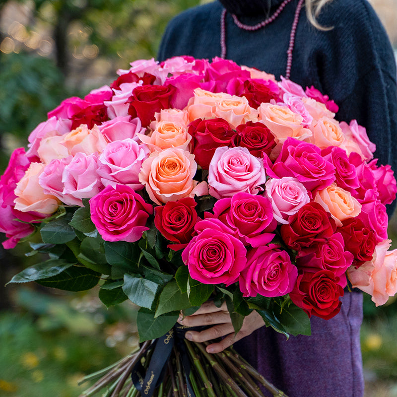 Bouquet of pink, red, and orange roses held by a person outdoors.