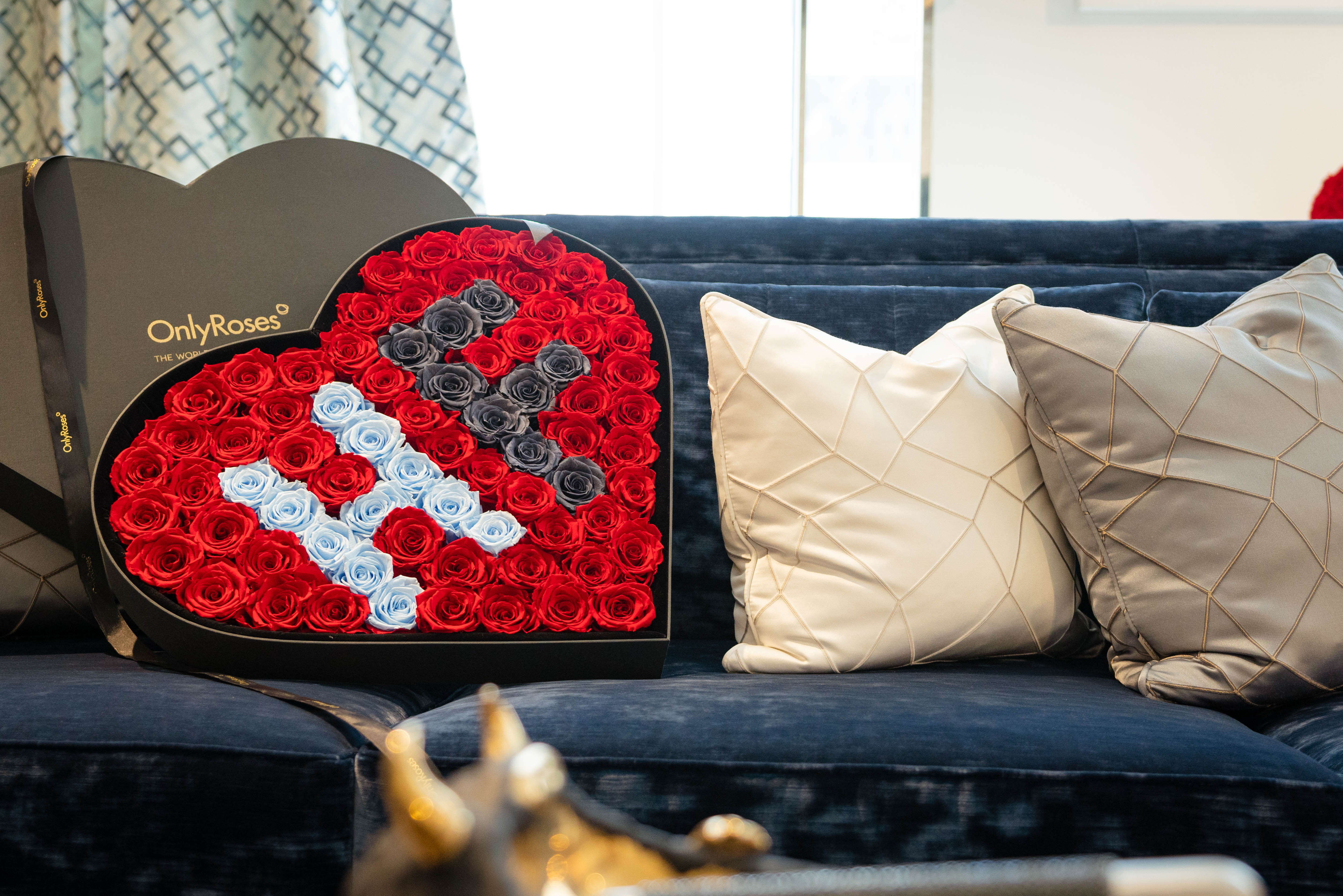 Heart-shaped arrangement of red roses with a logo on a blue couch