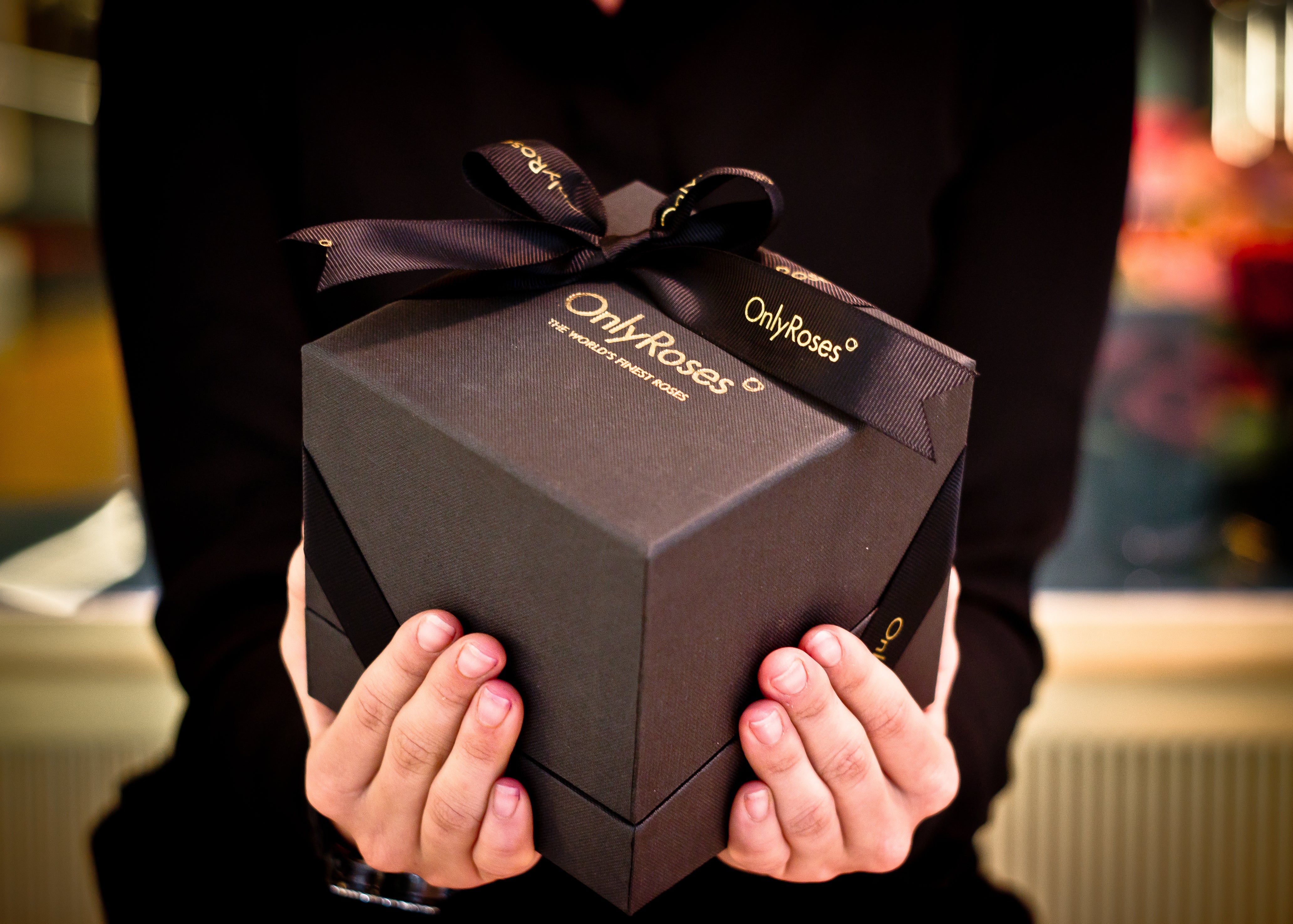 Person holding a black 'Only Roses' gift box with a bow.