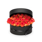 Black round box filled with red and orange roses on a white background