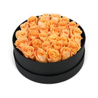 Black round box filled with peach roses on a white background
