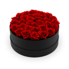 Black round box filled with red roses on a white background