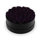 Black round box filled with dark purple roses on a white background