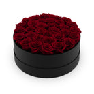 Black round box filled with red roses on a white background
