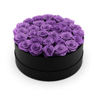 Black round box filled with purple roses on a white background
