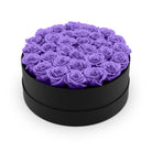 Black round box filled with purple roses on a white background