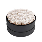 Black round box filled with white roses on a white background