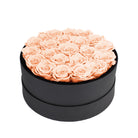 Black round box filled with peach roses on a white background
