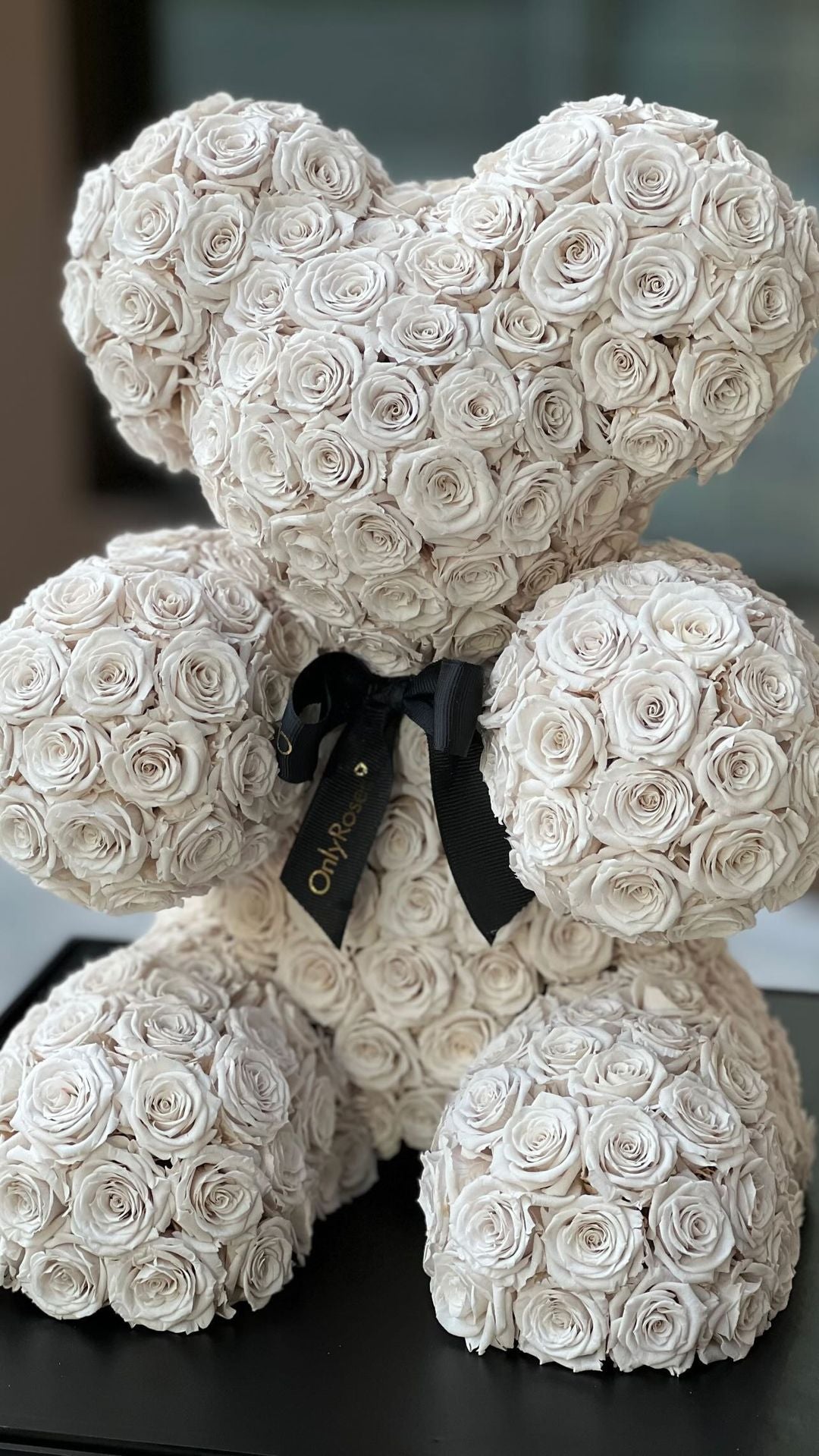 Teddy bear made of white roses with a black ribbon on a dark surface.