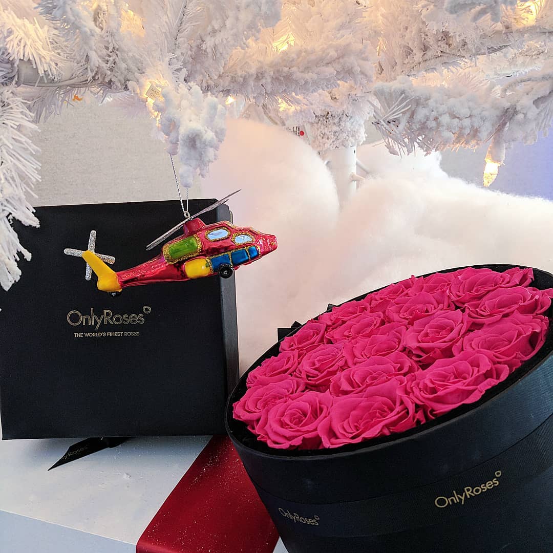 Heart-shaped box of pink roses with a toy helicopter and 'OnlyRoses' branding under a white Christmas tree.