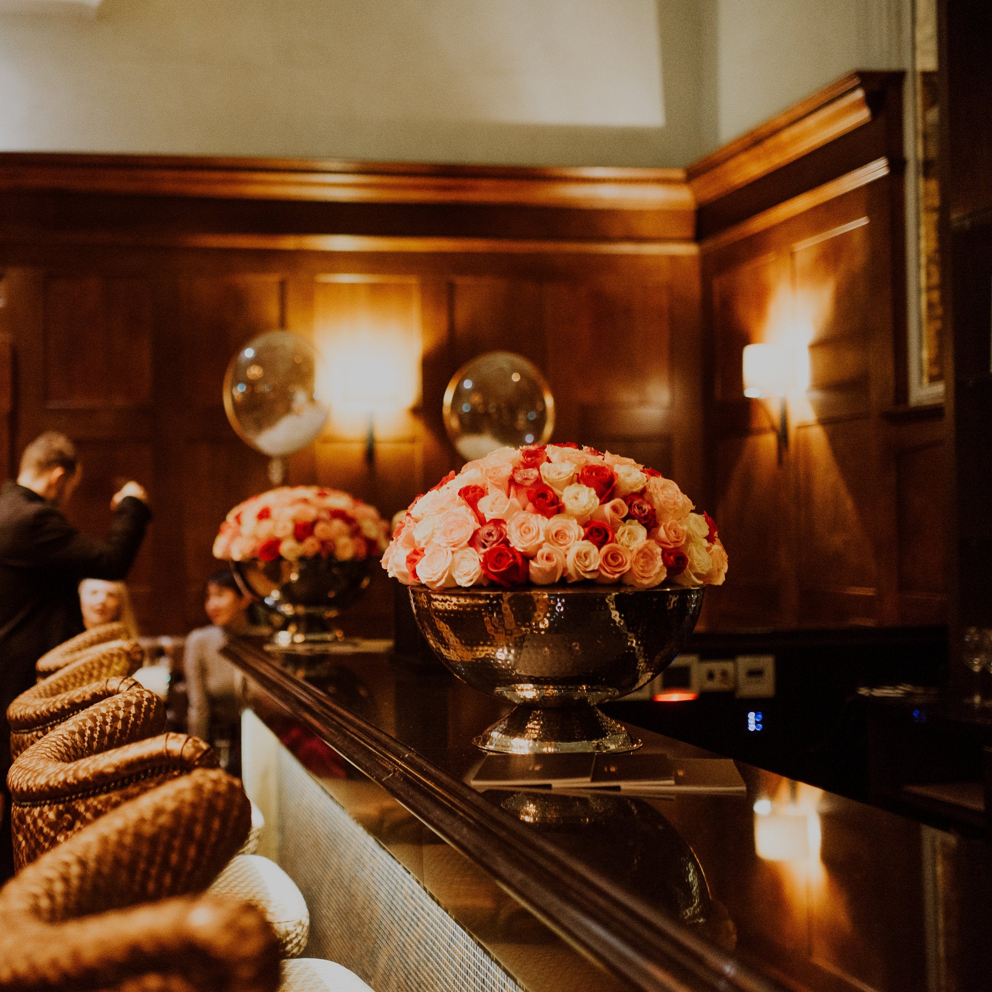Decorative floral arrangements on a bar counter with wooden paneling in the background. Chamagne Bowls