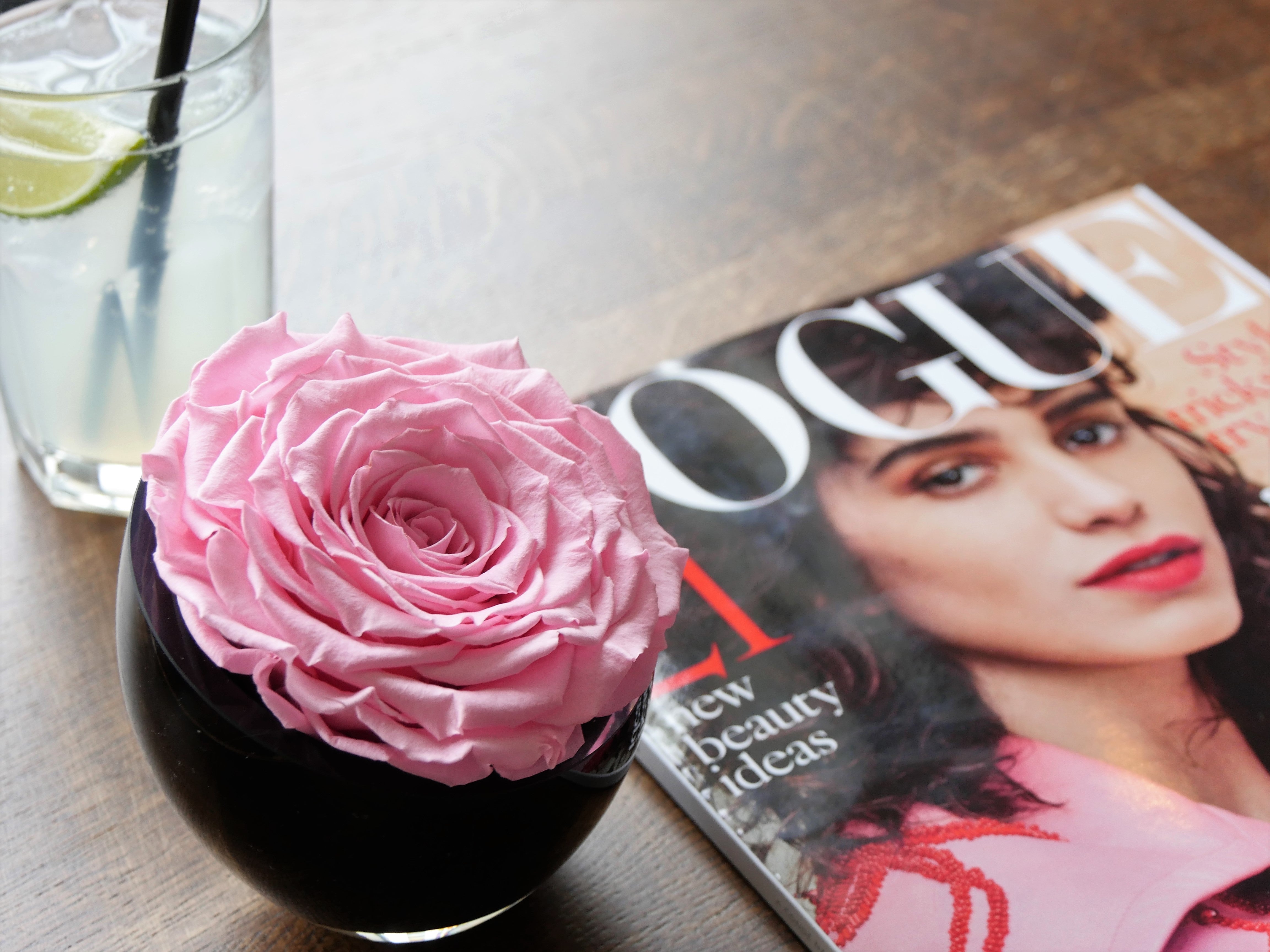 Pink rose in a glass with a magazine featuring a woman on a wooden surface
